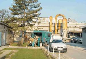 Obrázok - názov: Odber vzorky podz. vody pred neutralizačnou stanicou. V pozadí je hlavná výrobná hala.